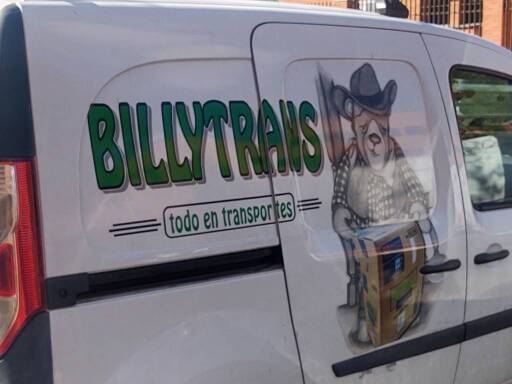 foto del costado de un vehículo de transporte con la leyenda en mayúsculas BILLYTRANS. abajo pone "todo en transportes" y al lado hay una ilustración de un oso vestido de leñador cargando una caja.